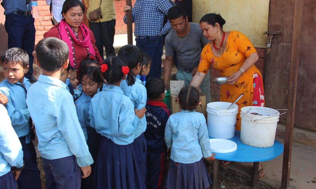 Mothers of the school kitchen ladle rice and lentils into steel bowls for the queue of children at the Bhimtar partner school.